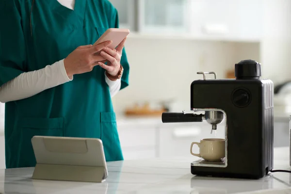 Nurse checking notifications on social media when making morning coffee
