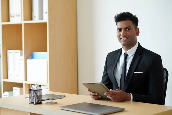 Portrait of cheerful Indian entrepreneur working on tablet computer at office desk