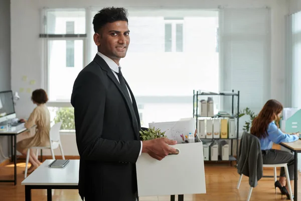 Smiling project manager bringing box with his belongings to office workplace