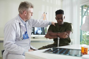 Askeri harekâta katıldıktan sonra ağır depresyon geçiren siyah askerin omzuna dokunan doktor.