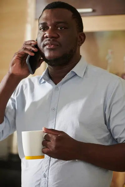 Anxious Black man drinking coffee and coffee talking on phone with coworker or employee