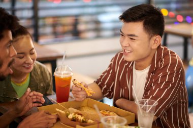 Neşeli Vietnamlı genç adam arkadaşlarıyla zaman geçiriyor pizza yiyor ve konuşuyor.