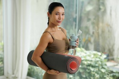 Gülümseyen sağlıklı kadının portresi yoga minderi ve bir şişe suyla.