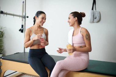 Gülümseyen sporcu kadınlar antrenmandan sonra vitamin içecekleri içiyorlar.