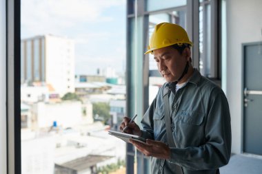 İnşaat alanında çalışırken kasket takan müteahhit, tablet bilgisayarda form dolduruyor