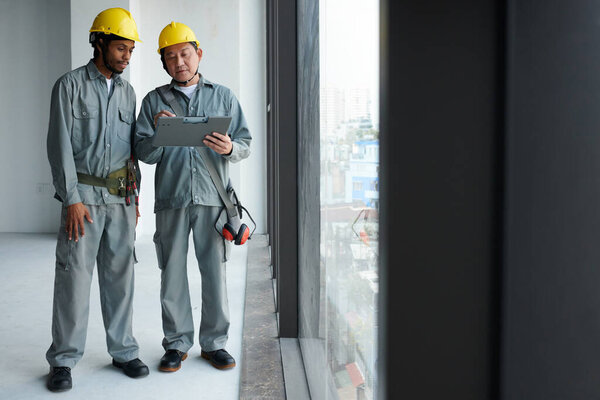 Construction workers discussing building blueprint on clipboard
