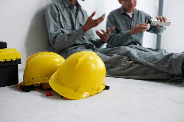 Two yellow hardhats on floor next to builders discussing work