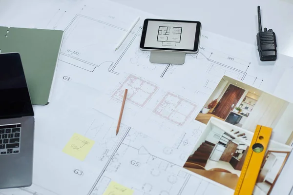 Tablet computer, photos, laptop and construction level on apartment floor blueprint