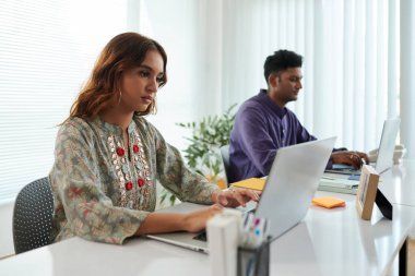 Ofiste dizüstü bilgisayarda çalışan ciddi Hintli genç bir kadın müşterilerden gelen e-postaları cevaplıyor.