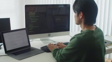 Ofisteki bilgisayarın önünde otururken arka plandaki erkek geliştiricinin kod yazma görüntüsü