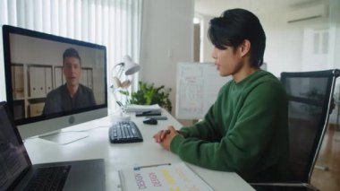 Erkek girişimcinin ofiste bilgisayar kullanarak iş ortağıyla yaptığı video konferansının yan görüntüsü