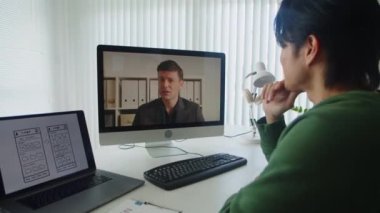 Çocuk müteahhitin iş arkadaşıyla video görüşmesinin arka planında bilgisayar başında oturuyor.