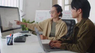 Yeni projeyle ilgili fikirleri paylaşan kadın programcı ile erkek meslektaşının ofiste bilgisayar monitörü önünde dizüstü bilgisayarda çalışırken orta boy görüntüsü.