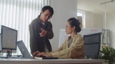 Erkek kıdemli kodlayıcının, modern ofiste dizüstü bilgisayarda çalışan yeni bir çalışana talimat verirken orta uzunlukta bir fotoğrafı.