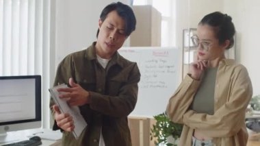 Erkek takım liderinin, ofisteki iş kâğıdını kullanarak bilişim projesindeki görevler hakkında kadın grafik tasarımcısıyla iletişim kurduğu orta boy bir fotoğraf.