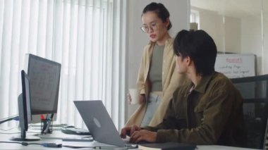 Yeni erkek kodlayıcıya rehberlik eden ve dizüstü bilgisayar kullanarak uygulamanın geliştirilmesine yardımcı olan kadın eğitmenin orta uzun yavaşlığı