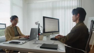 Modern ofiste bilgisayar ve dizüstü bilgisayar kullanarak yazılım geliştirme sırasında kodlar üzerinde çalışan iki Asyalı programcının orta uzunluktaki görüntüsü.