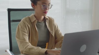 Dizüstü bilgisayarda çalışan neşeli Asyalı kadın kodcunun yavaş yavaş portresini kaldır. Ofiste oturmuş kameraya bakıyorsun.