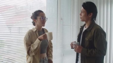 İki Asyalı iş arkadaşının mesai saatleri boyunca haberleri tartışırken ve kahve içerken orta ölçekli bir fotoğrafı.