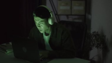 Gece geç saatlerde dizüstü bilgisayarda çalışırken kulaklık takan düşünceli bir erkek müteahhit.