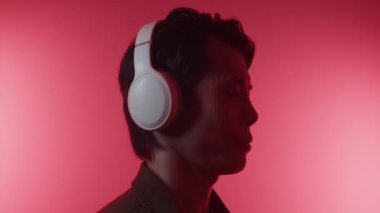 Kulaklık takan neşeli Asyalı adamın yakın plan portresi. Kameraya bakıyor, kırmızı LED, gösterişsiz.