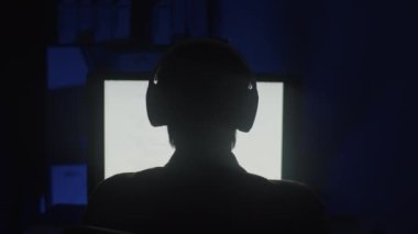 Gece geç saatlerde kodlama yaparken büyük ekranın önünde oturan kulaklık takan kişinin arka görüntüsü