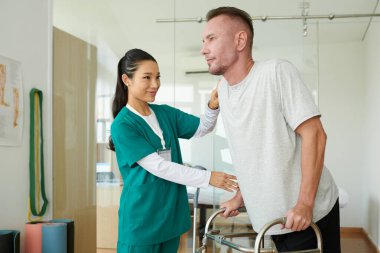 Olgun bir adam, aylaklarla rehabilitasyon hemşiresinin kontrolünde olmayı öğreniyor.