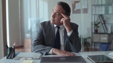 Modern ofiste masa başında otururken baş ağrısı çeken yaşlı erkek girişimcinin orta boy fotoğrafı.