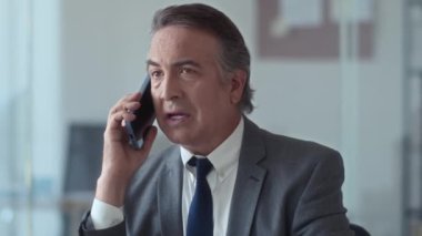 Üst düzey iş adamının iş yerinde iş arkadaşıyla cep telefonuyla konuşurken orta yavaş bir görüntüsü.