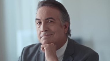 Ofiste çalışırken kameraya bakan gülümseyen erkek yöneticinin orta boy yakın portresi.