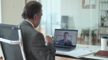 Üst düzey yöneticinin yeni iş projesinin detaylarını paylaşırken görüntülü konuşma sırasında ofiste dizüstü bilgisayarın önünde oturuyor.