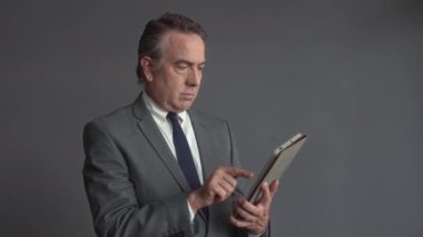 Dijital tablet kullanan ve kameraya bakan gülümseyen yaşlı işadamının orta boy portresi