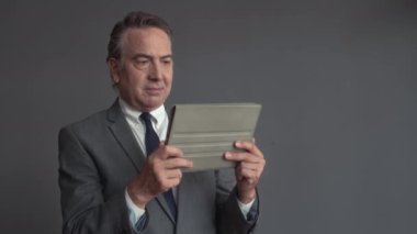 İş elbisesi içinde kablosuz dijital tablet üzerinde çalışan olgun girişimcinin orta ölçekli fotoğrafı.