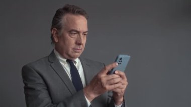 Yetişkin bir ofis çalışanının kapalı alandaki gri duvar arkaplanlı akıllı telefondan mesaj gönderirken orta boy görüntüsü.