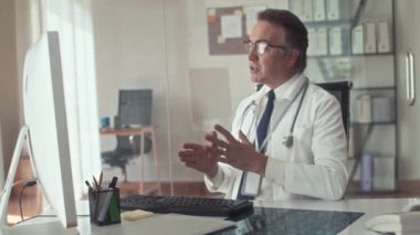 Orta yaşlı terapistin videoda hastayı arayıp klinikteki bilgisayarın önünde ilaç yazması.