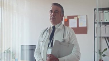 Üst düzey terapistin elinde hasta kartıyla kameraya bakarken orta boy portresi.