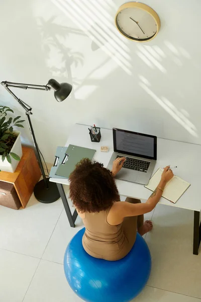 Woman sitting on fitness ball at desk in home office when learning coding