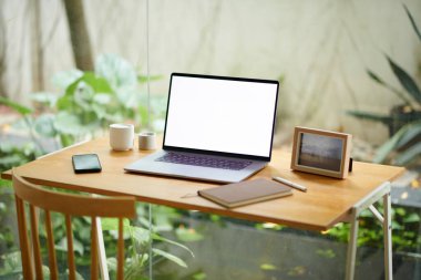 Ev ofisinin minimalist masasındaki boş ekranlı dizüstü bilgisayar mumlar ve resim çerçevesi ile dekore edilmiş.