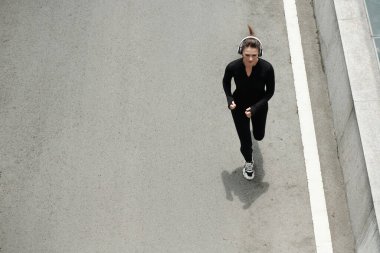 Sokak boyunca müzik eşliğinde koşan, kablosuz kulaklıklı genç bir kadının yüksek açılı görüntüsü.