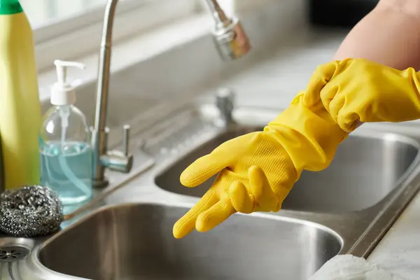 Close-up of young woman in protective gloves washing dishes in sink in kitchen