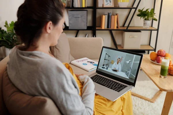 거실에서 소파에 앉아있는 노트북을 그녀의 의사와 온라인으로 이야기 — 스톡 사진