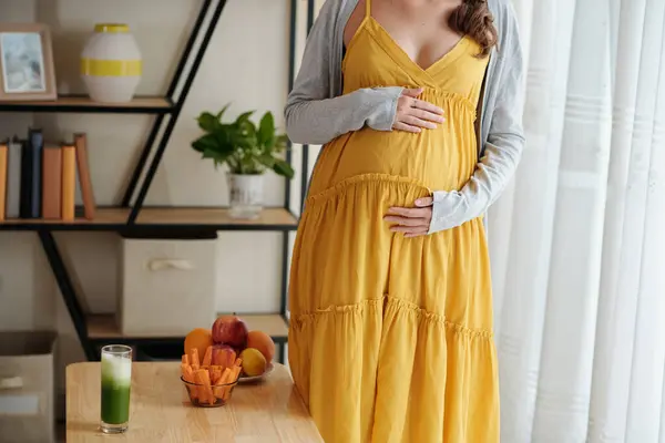身着黄色衣服的孕妇站在客厅里抚摸怀孕的肚子的特写 — 图库照片