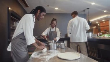 Restoran mutfağında iş arkadaşlarıyla birlikte yemek pişirirken orta boy Afro-Amerikan pastanecinin çiğ hamur ezdiği bir fotoğraf.