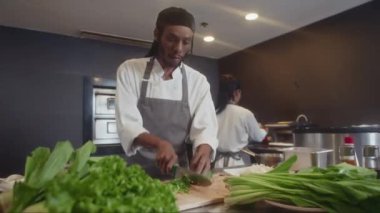Kafe mutfağında iş arkadaşlarıyla pano pişirme salatasında soğan doğrayan siyah aşçının düşük açılı görüntüsü.