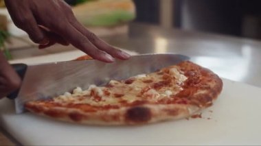 Mutfak masasında yeni pişmiş peynirli domatesli pizzayı dilimleyen aşçının ellerini kapatın.