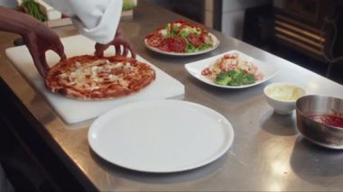 Domatesli pizzayı tabağa koyup restoranda servis için yemek hazırlayan tanınmamış aşçı yamağı.