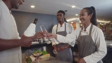 Dost canlısı, çok ırklı şeflerden oluşan bir ekip restoranda mesainin bitmesini kutluyor ve bardaklara şarap dolduruyor.