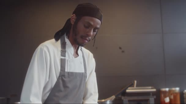 カフェのキッチンで料理する料理のためのチーズをグレーティングエプロンでアフリカ系アメリカ人のシェフのチルトダウンショット — ストック動画