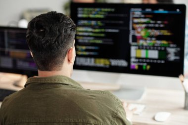 Bilgisayar ekranında programlama koduna bakan yazılım geliştiricisi, arkadan görünüm