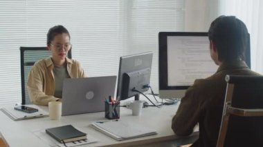 Bilgisayar ve dizüstü bilgisayarda çalışan iki Asyalı geliştiricinin modern ofiste masasında otururken orta uzunlukta bir fotoğrafı.
